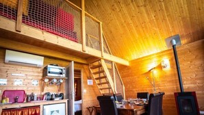 A cozy cabin with a wooden interior, a dining area with chairs, a small kitchen with a refrigerator, and a staircase leading to a loft area. - Safari.... (Le Vigen)
