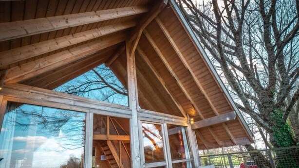 A wooden-roofed covered patio with wicker furniture and a glass door leading to an interior space. - Safari.... (Le Vigen)