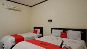 Ein Hotelzimmer mit zwei Betten, jeweils mit weißer Bettwäsche und roten Akzenten, einem kleinen Nachttisch sowie einer Wand-Klimaanlage.