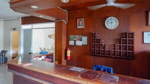 Una zona de recepción con un mostrador de madera, un reloj, un cuadro enmarcado y un extintor.
