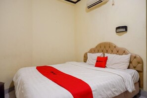Una camera d'albergo con un letto, una coperta rossa, una testiera bianca e un condizionatore d'aria.