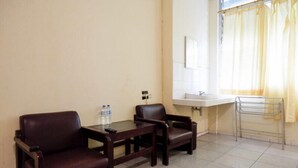 Ein kleines, sauberes Zimmer mit einer Couch, einem Tisch, einem Waschbecken und einem Fenster mit Vorhängen.