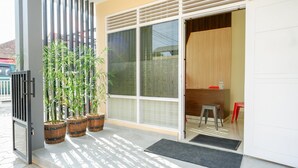 Una entrada moderna con puerta corredera de vidrio, plantas en macetas, un taburete pequeño y un felpudo.