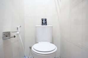 A white toilet with a toilet paper holder and a bidet attachment. - Reddoorz Near Gejayan 3 (Depok)