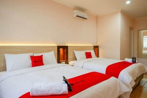 A hotel room with two beds, each with white bedding and red accents, a wooden headboard, and an air conditioning unit on the wall. - Reddoorz Near Gejayan 3 (Depok)
