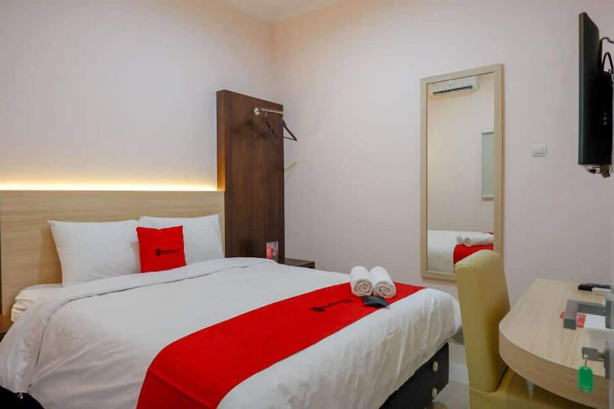 A hotel room with a bed, a desk, a mirror, and a wardrobe.