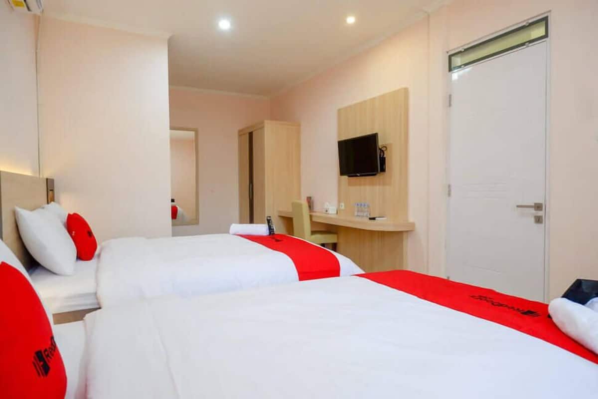 A hotel room with two beds, a desk, a television, and a door.