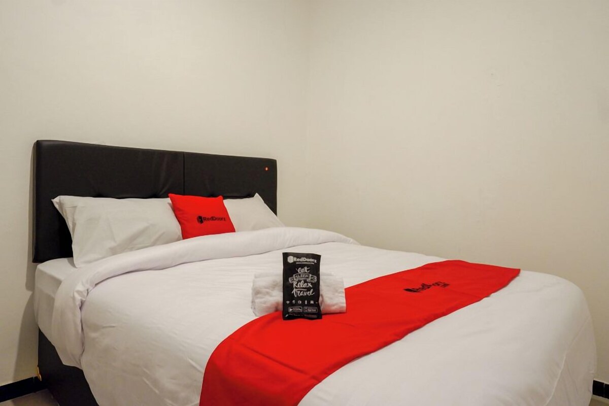 Ein ordentlich bezogenes Bett mit weißer und roter Bettwäsche, einem roten Kissen und einem Relax Travel Handtuch von RedDoor.