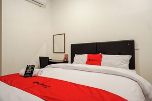 A neatly made bed with white and red bedding, a black headboard, and a small bedside table with a lamp and a book. - Reddoorz @ Jalan Wonosari Km.9 (Yogyakarta)