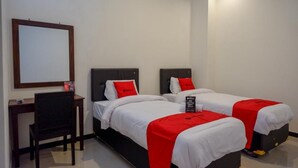 A hotel room with two single beds, each with a red blanket and pillow, a desk with a chair, and a large mirror on the wall. - Reddoorz @ Jalan Wonosari Km.9 (Yogyakarta)