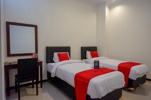 A hotel room with two single beds, each with a red blanket and pillow, a desk with a chair, and a large mirror on the wall. - Reddoorz @ Jalan Wonosari Km.9 (Yogyakarta)