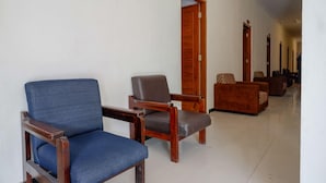 A hotel lobby with a blue armchair, a wooden chair with a cushion, and a patterned sofa. - Reddoorz @ Jalan Wonosari Km.9 (Yogyakarta)