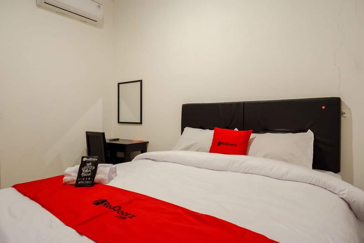 A hotel room with a bed, a nightstand, a framed picture on the wall, and a red blanket with the hotel logo.