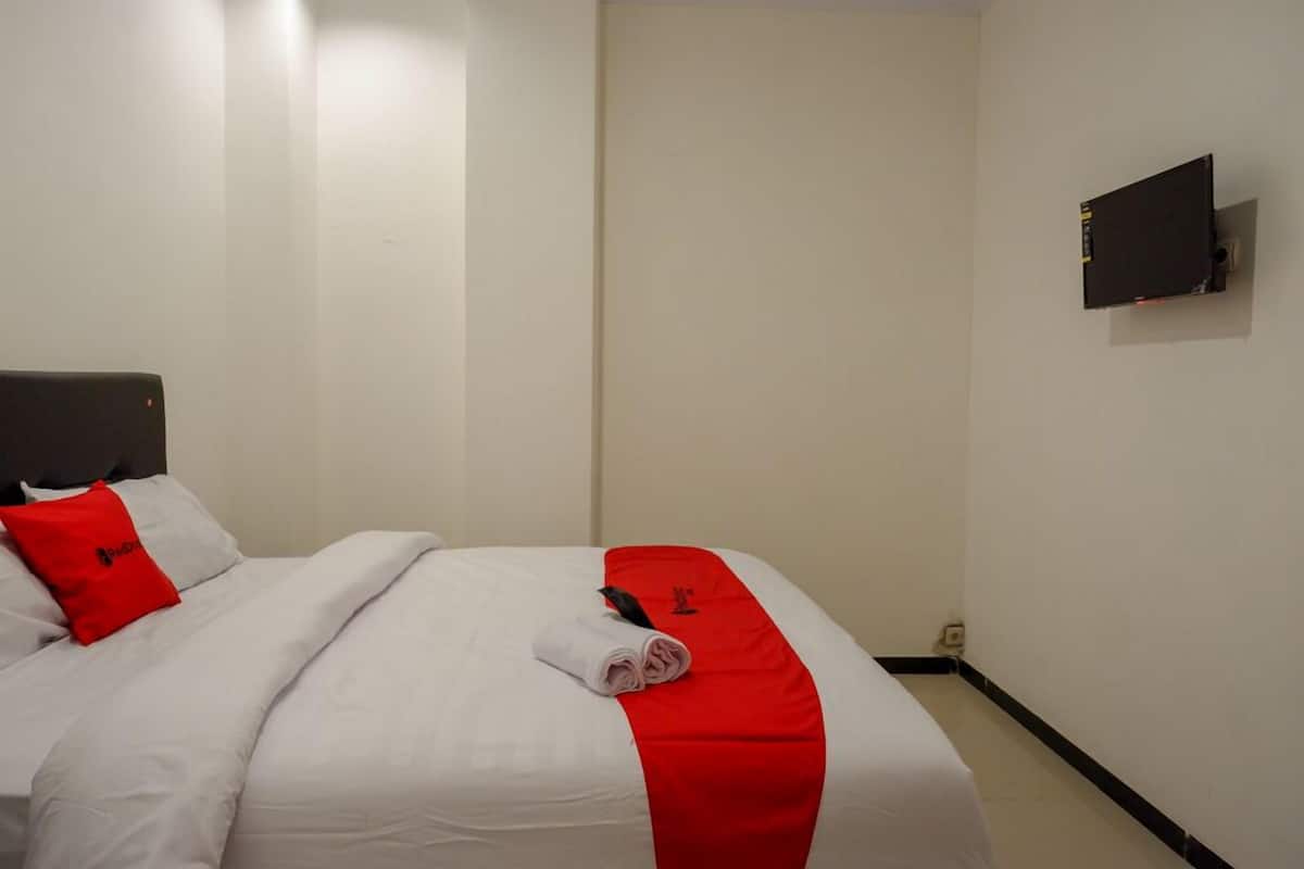 A hotel room with a bed, a TV mounted on the wall, and a red and white bedspread.
