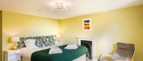 A bedroom with a bed, bedside lamps, a green throw blanket, a chair, and a fireplace.