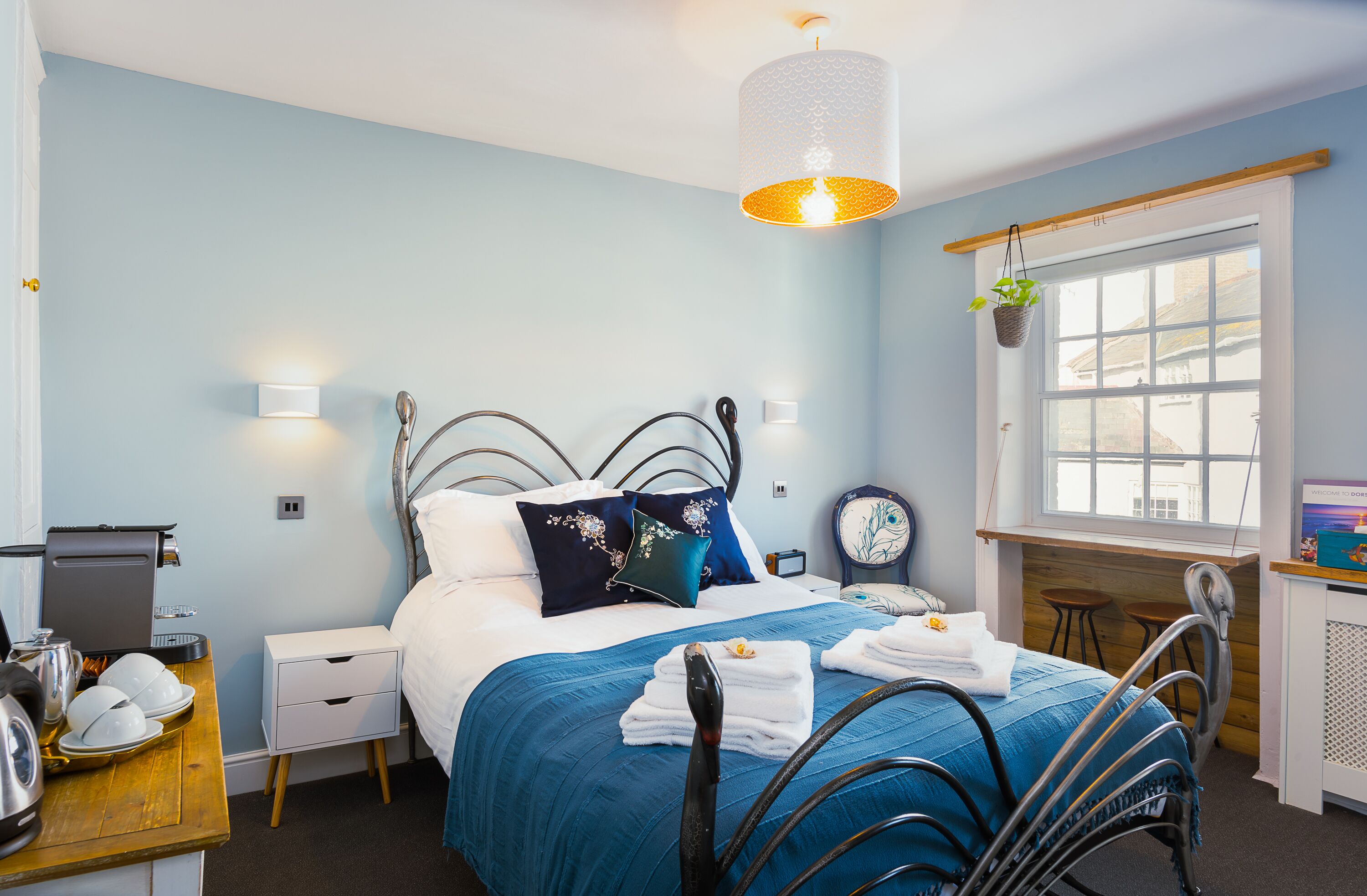 A neatly arranged bedroom with a bed, bedside tables, a desk, and a window with a view.