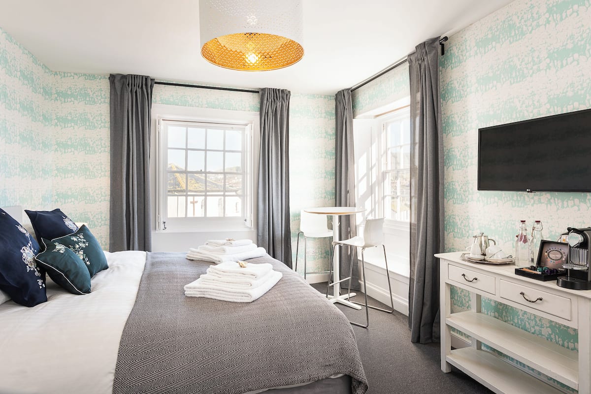 A neatly made bed with towels, a bedside table with a lamp, and a TV on the wall.
