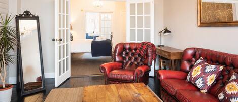 A living room with a red leather sofa, a matching armchair, a wooden coffee table, and a large mirror.