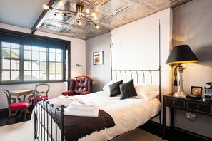 A neatly arranged bedroom with a large bed, a chair, a desk, and a lamp.