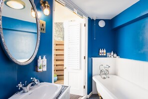 A bathroom with a white sink, a bathtub, and a large mirror. There are toiletries on the wall and a wooden door leading outside.