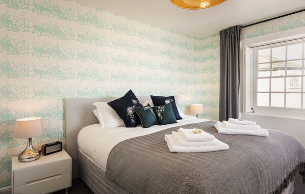 A neatly made bed with a patterned bedspread, two pillows with floral designs, and folded towels on the bed. - Lyme 1 Hotel (Lyme Regis)