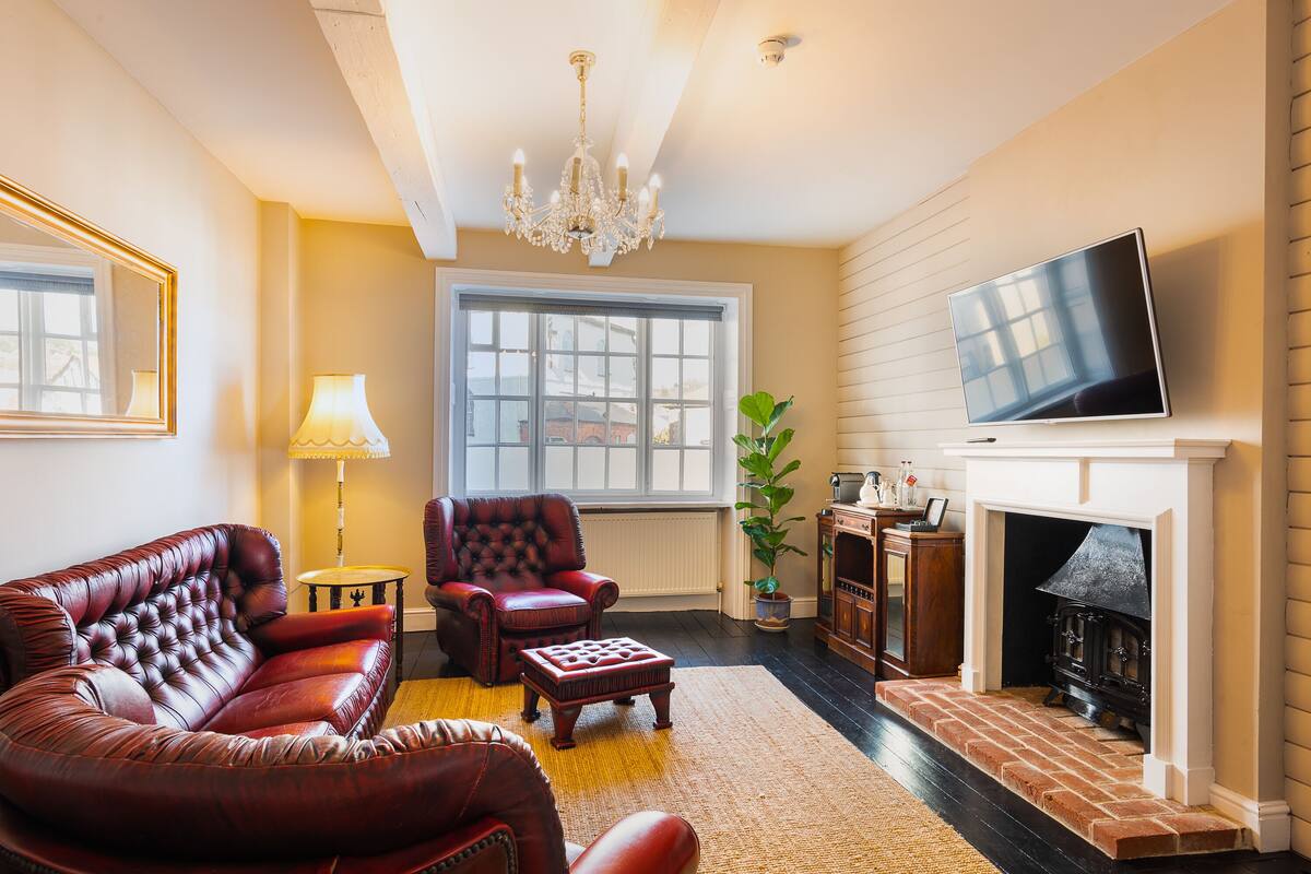 A living room with a fireplace, leather sofa, armchair, and a television mounted on the wall.