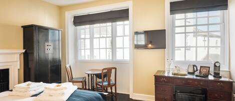 A hotel room with a bed, a desk, a dresser, a television, and a fireplace.