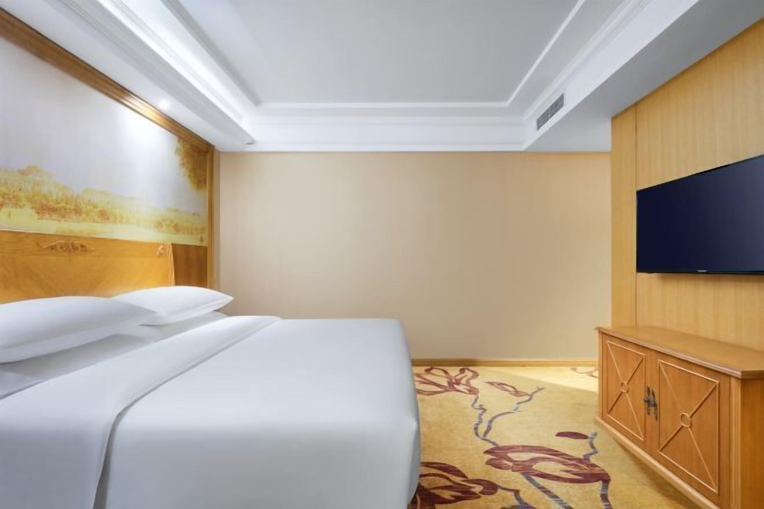 A hotel room with a bed, a television, and a wooden cabinet.