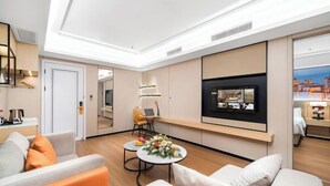 Une chambre d’hôtel moderne avec un canapé, une table basse ronde agrémentée de fleurs, un téléviseur fixé au mur et une vue sur la ville.