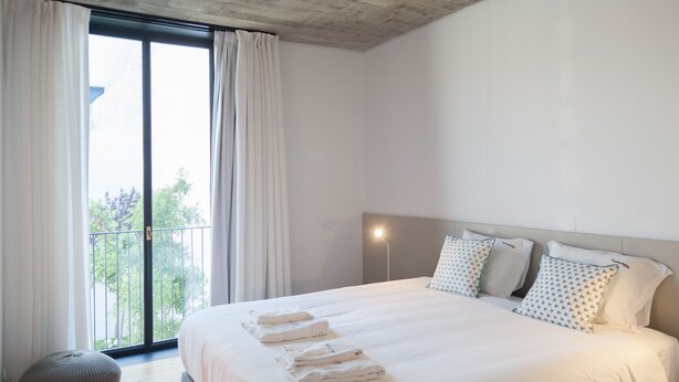 Ein modernes Hotelzimmer mit einem großen Bett, einem Balkon mit Vorhängen und Blick auf Grünflächen.