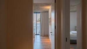 Ein Flur, der zu einem Schlafzimmer mit Bett, einem fenster mit Vorhängen und einem Balkon mit Blick auf Palmen führt.