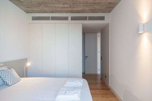 A modern hotel room with a large bed, white walls, a wooden floor, and a closet with sliding doors. - FLH Intendente Cozy Industrial Flat (Lisbon)