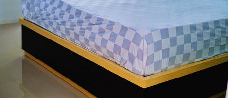 A bed with a checkered mattress in a room with a wooden headboard and a window with a view of greenery.