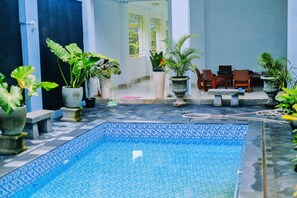 A pool area with tiled flooring, potted plants, and wooden furniture. - Reddoorz @ Artomoro Guest House (Sleman)