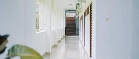 Un pasillo con una escalera al final, paredes blancas y suelo de baldosas.