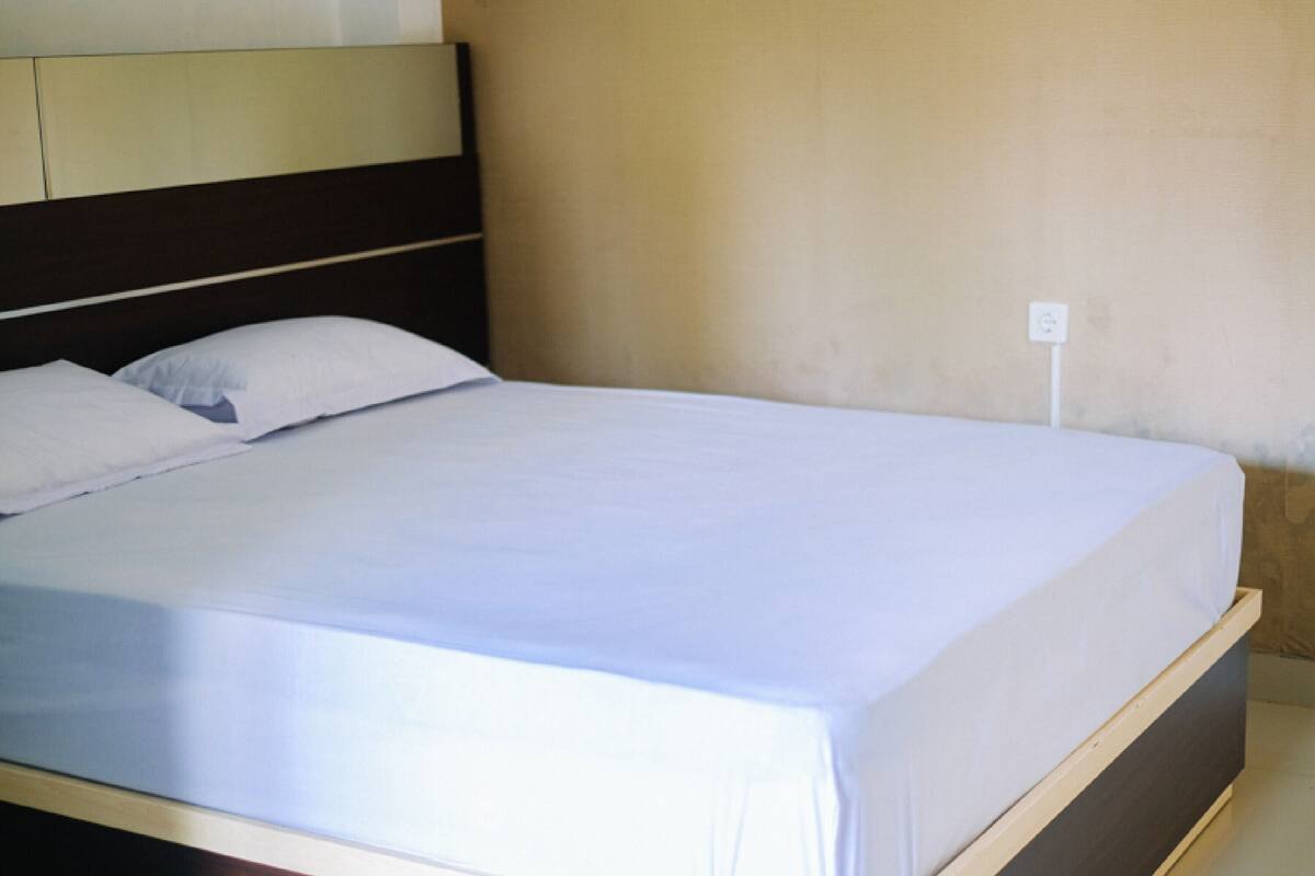 Ein Bett mit weißen Laken, einem Holzkopfstück und einer schlichten Wand mit Steckdose.