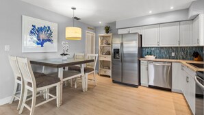 Une cuisine moderne avec des meubles blancs, un réfrigérateur en acier inoxydable et une table à manger en bois, assortie de chaises.