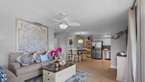 Un salon moderne avec un canapé, une table basse et des coussins décoratifs. On aperçoit à l’arrière-plan un coin repas avec des chaises et une table.