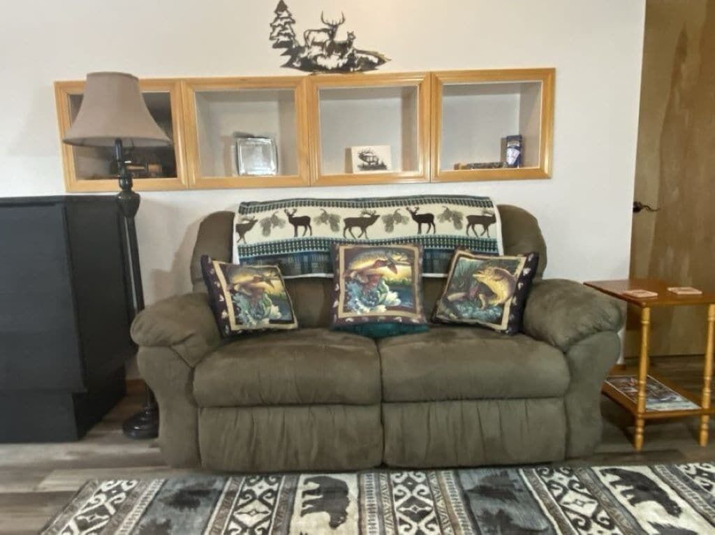 A living room with a sofa, a lamp, a rug, and a wall with framed pictures and shelves.
