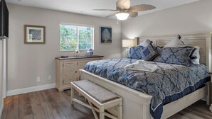 Une chambre à coucher comprenant un lit, un banc, un ventilateur de plafond, une fenêtre et une commode.