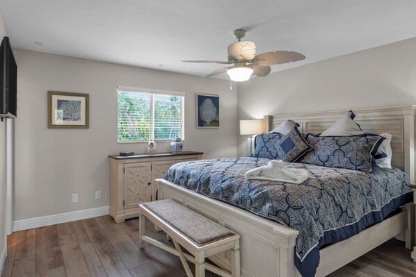 Un dormitorio con cama, banca, ventilador de techo, ventana y cómoda.
