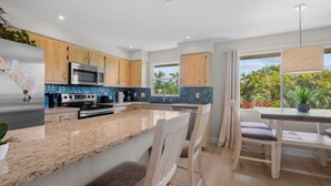 Une cuisine moderne dotée d’un îlot central, d’appareils électroménagers en acier inoxydable, de meubles de rangement en bois et offrant une vue sur la végétation tropicale.