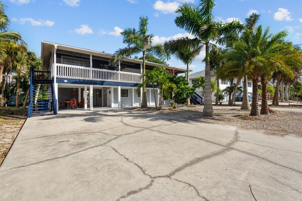 A two-story building with a balcony, palm trees, and a concrete driveway.