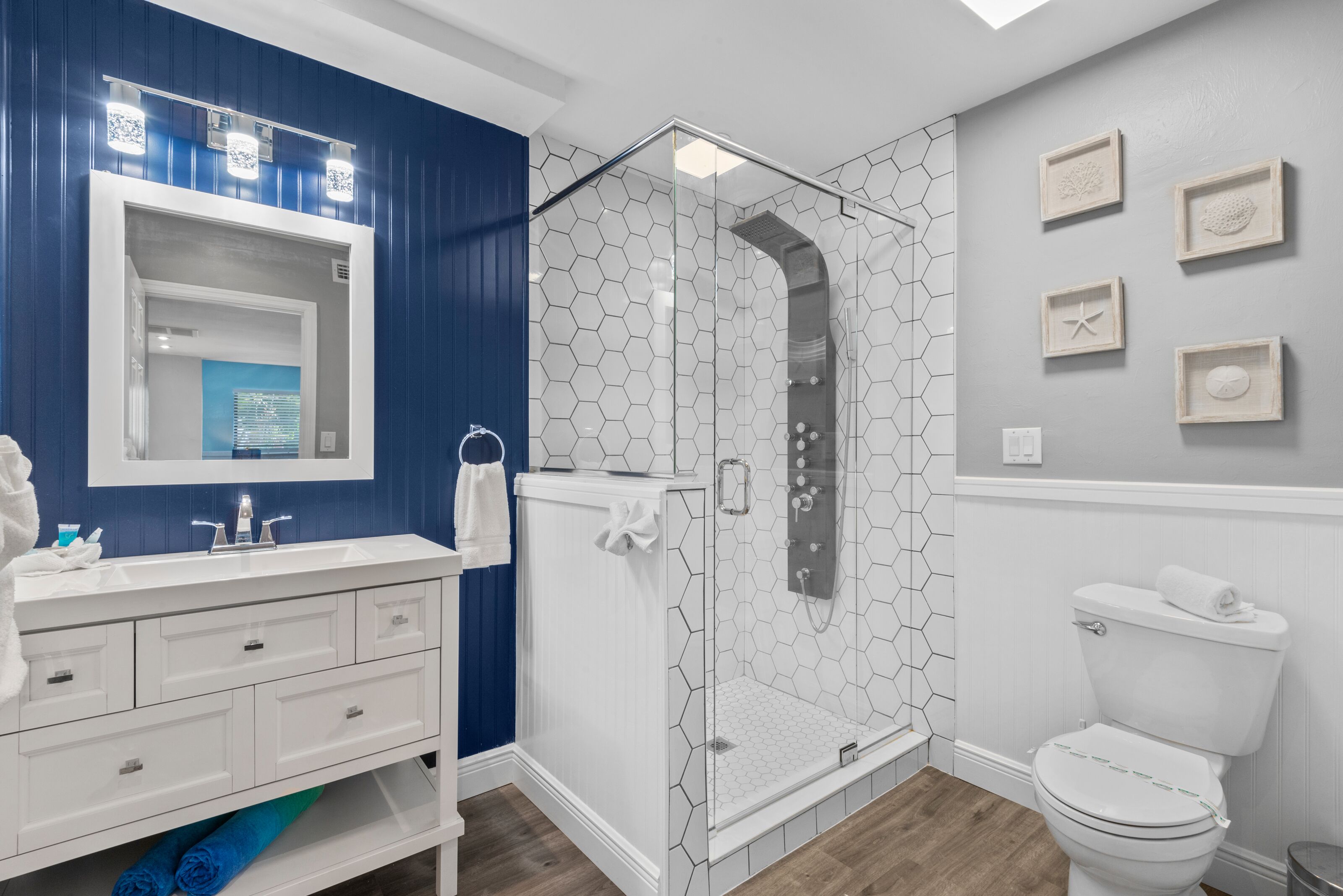 Un bagno moderno con un lavandino bianco, pareti blu, un box doccia in vetro e un water.