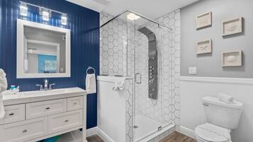 Un bagno moderno con un lavandino bianco, pareti blu, un box doccia in vetro e un water.