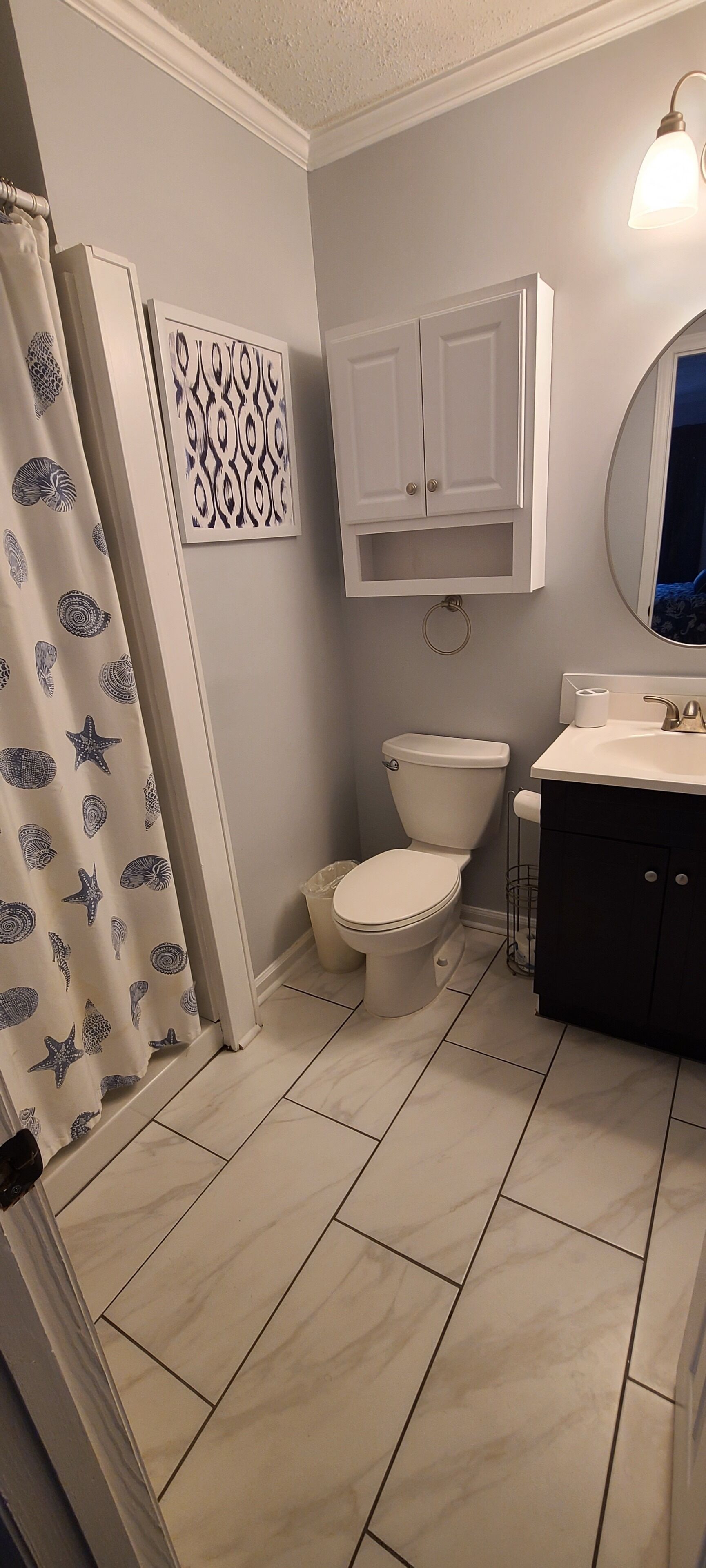 Et badeværelse med toilet, håndvask, spejl og bruseforhæng med et søskalsmønster.