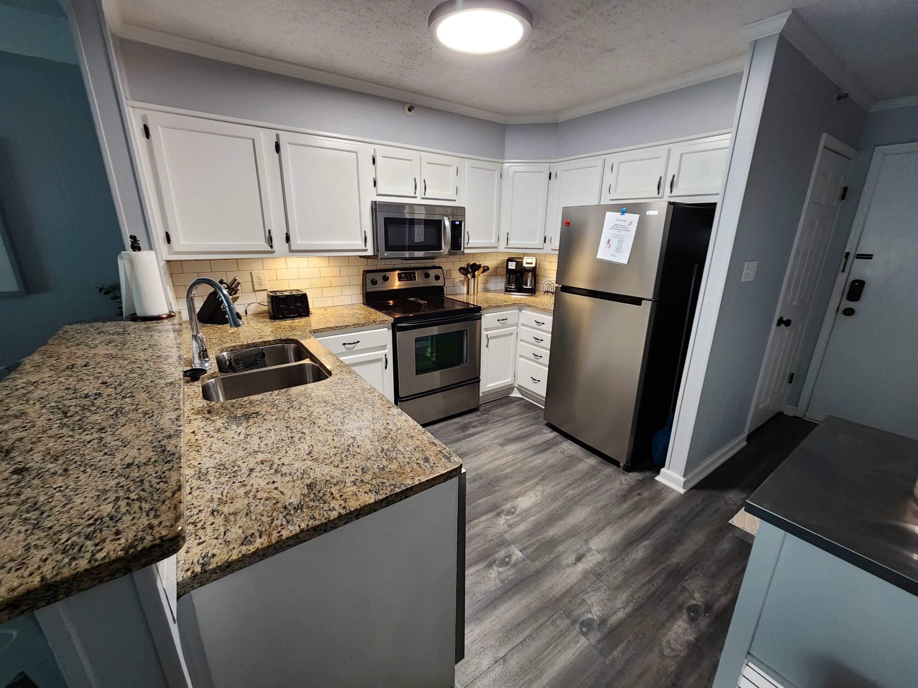 A modern kitchen with white cabinets, stainless steel appliances, granite countertops, and a wood floor.
