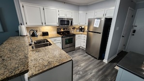 Una cocina moderna con armarios blancos, electrodomésticos de acero inoxidable, encimeras de granito y suelo de madera.