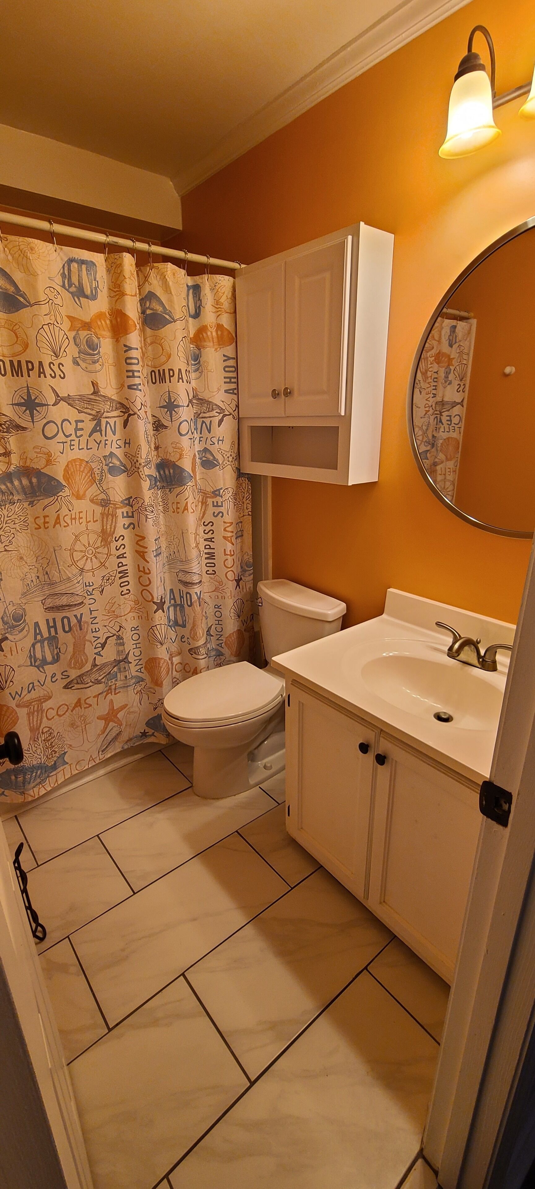 A bathroom with a toilet, sink, and a shower curtain with nautical designs.