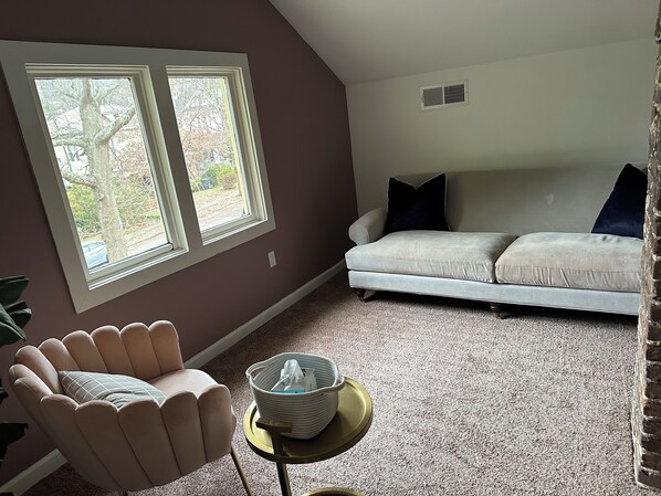 Un salón con un sofá color crema, un sillón rosa y una pequeña mesa redonda con una cesta.